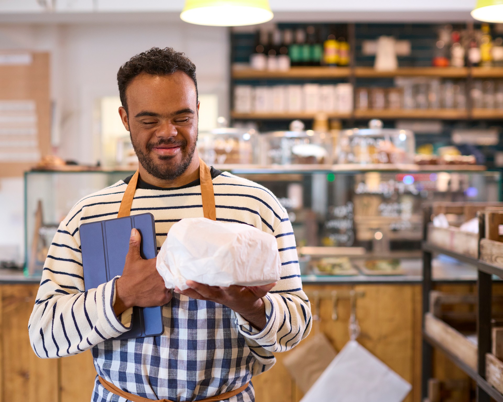 Smiling Man With Down Syndrome Working In Food Shop Using Digital Tablet